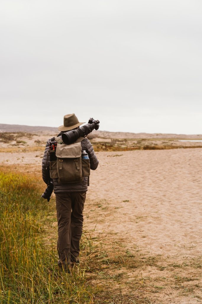 Back View Of Person Carrying Camera Equipment Walking on Sandy Ground